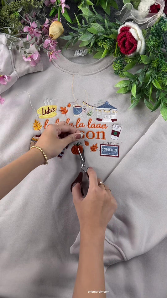 Hands using small embroidery scissors to cut loose threads on a custom La La La Season embroidered sweatshirt.