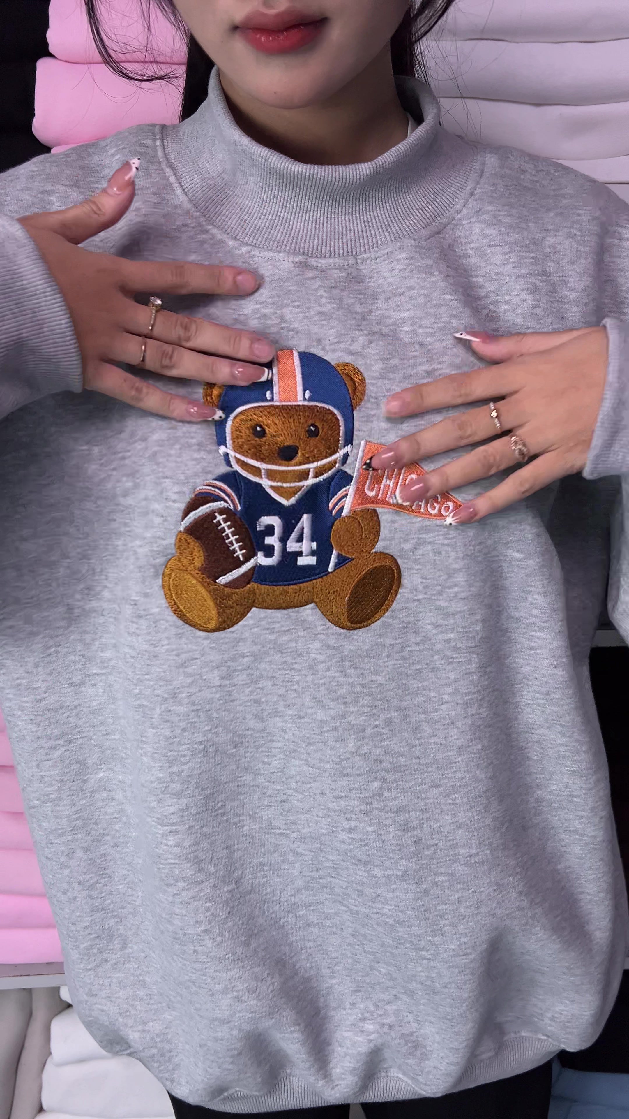 Video showing embroidered details of Chicago football teddy bear wearing helmet 34 holding football and pennant flag on a grey sweatshirt