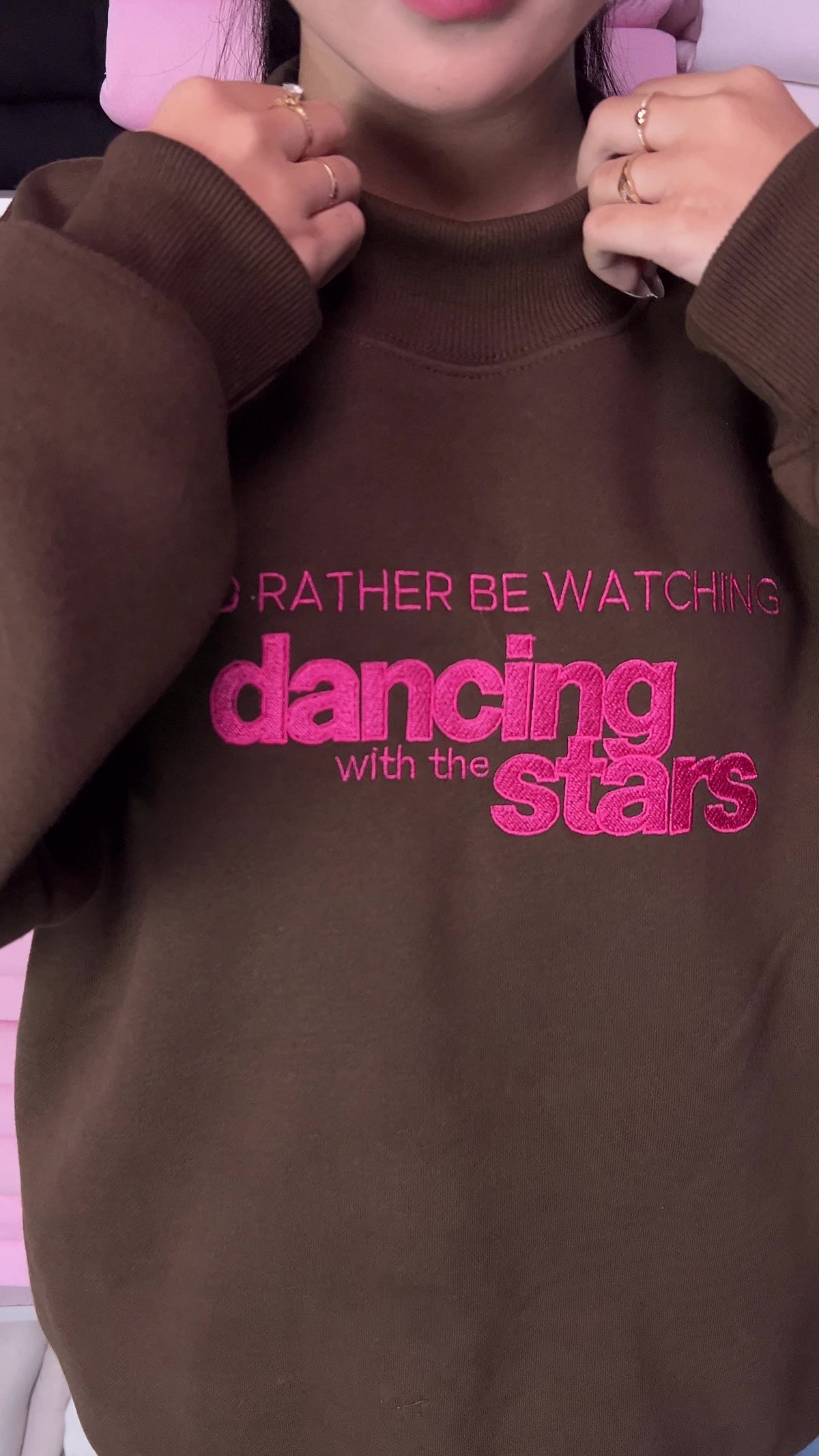 Video showing vibrant hot pink embroidery detail of I'd Rather Be Watching Dancing with the Stars on a brown sweatshirt