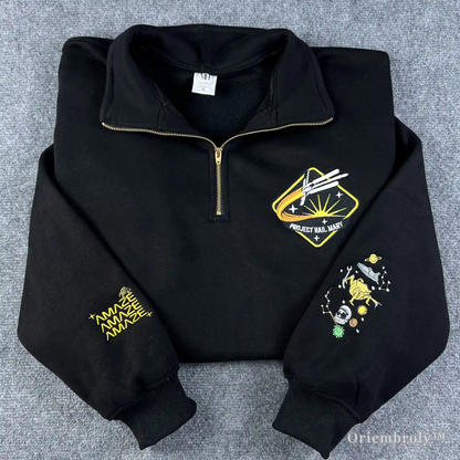 A high-quality black quarter-zip sweatshirt featuring embroidered Project Hail Mary mission patch and Rocky the Eridian illustration on the sleeve. Perfect gift for Andy Weir sci-fi fans and book lovers.