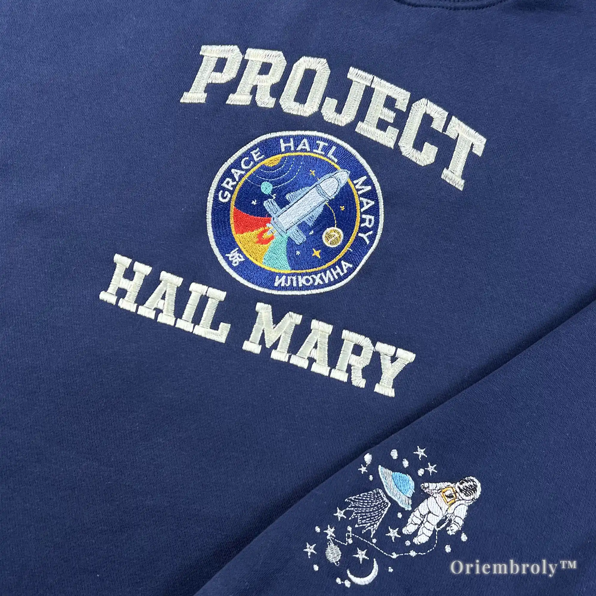 Close-up of a navy pullover featuring detailed sleeve embroidery of Rocky the Eridian and a floating astronaut. High-density satin stitching inspired by the scientific friendship in Project Hail Mary