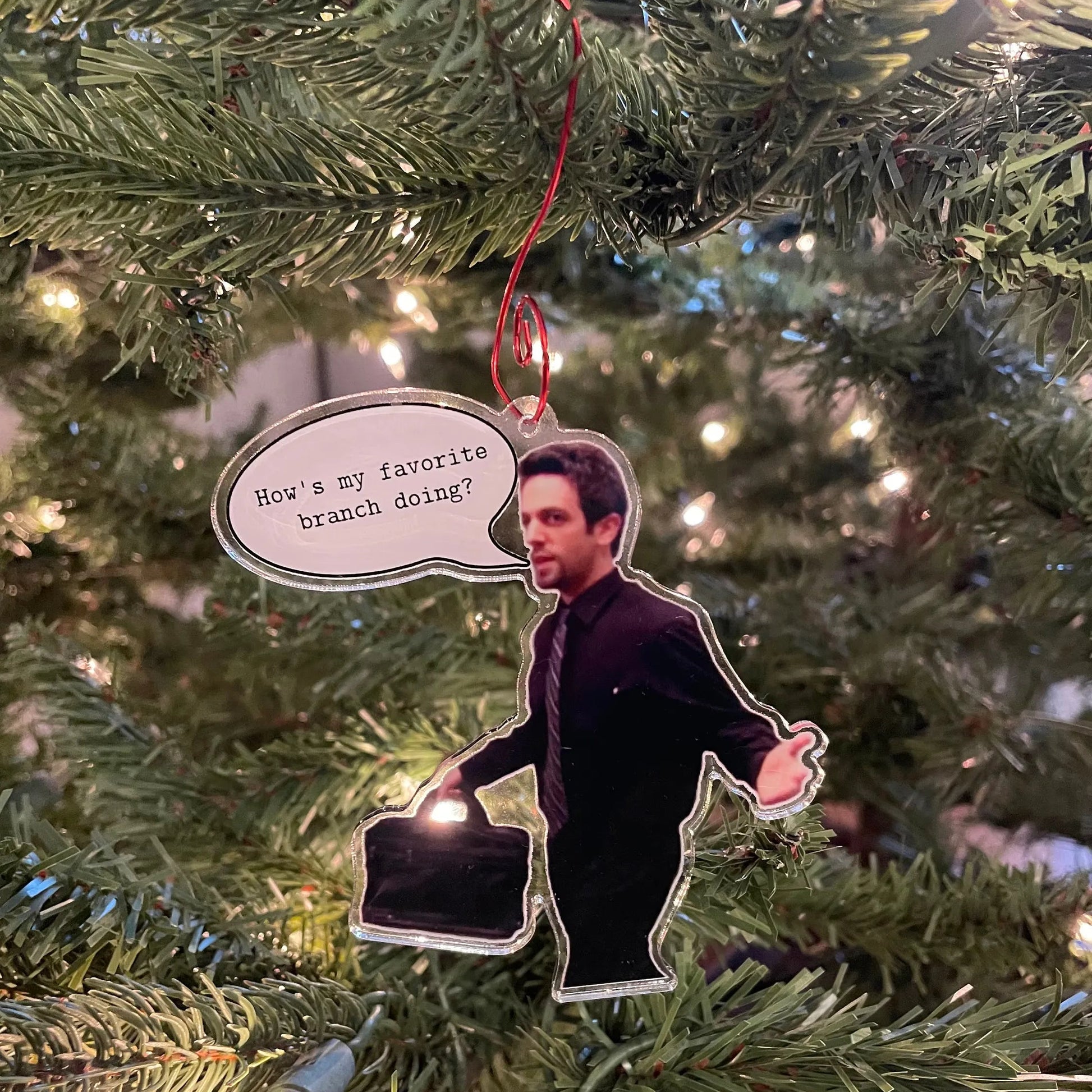 A Ryan Howard 'The Office' Christmas ornament hanging on a Christmas tree, featuring the quote 'How's my favorite branch doing?