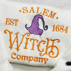 White pillow with 'Salem Est 1684 Witch Company' text and purple witch hat design on a light wooden surface.