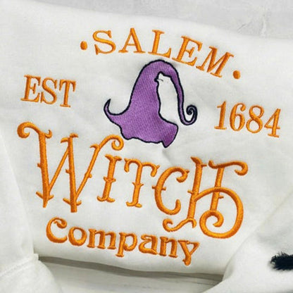 White pillow with 'Salem Est 1684 Witch Company' text and purple witch hat design on a light wooden surface.