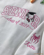 Close-up of pink SENIOR Class of 2027 embroidery with Spider-Man wearing a graduation cap and embroidered sleeve name.