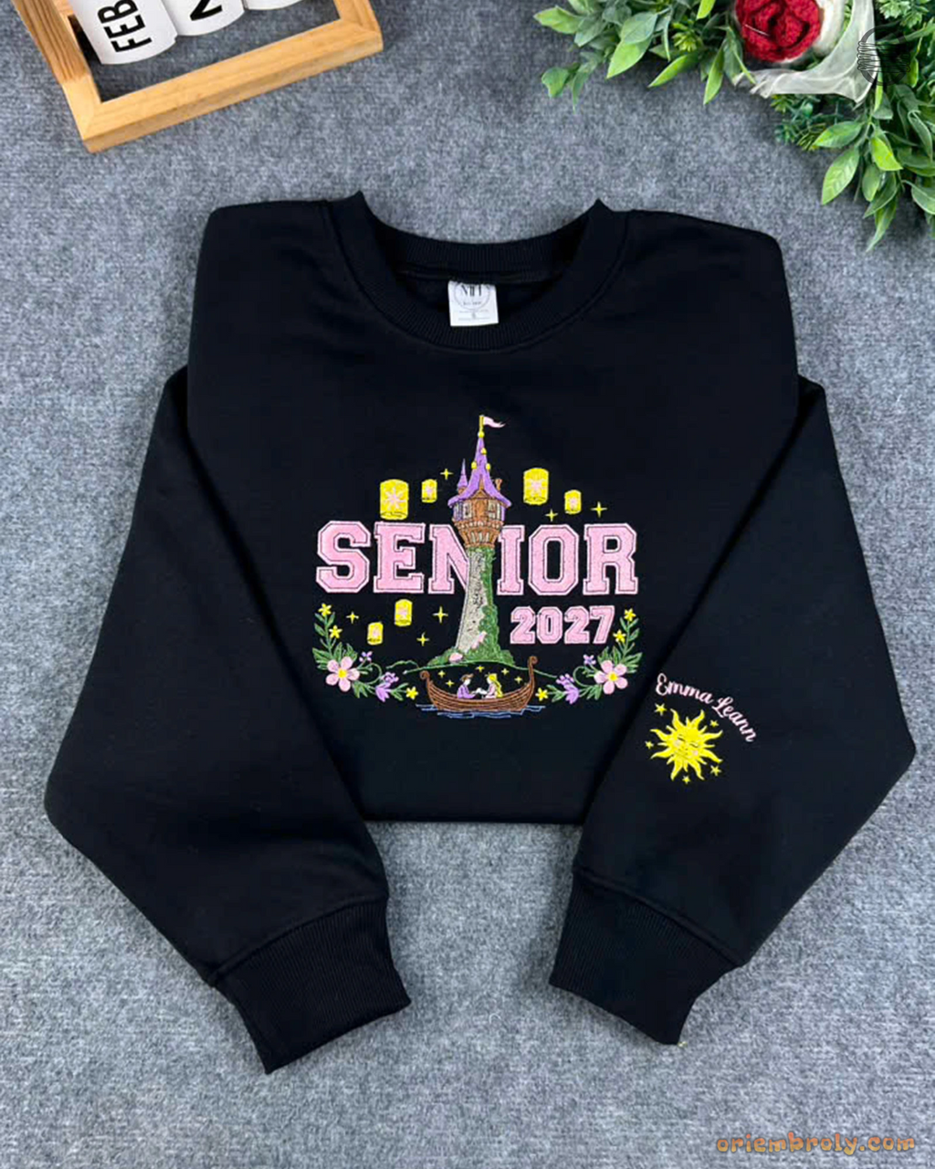 Flat lay of a black Senior 2027 sweatshirt featuring Tangled Rapunzel tower, floating lanterns, and sun emblem sleeve embroidery