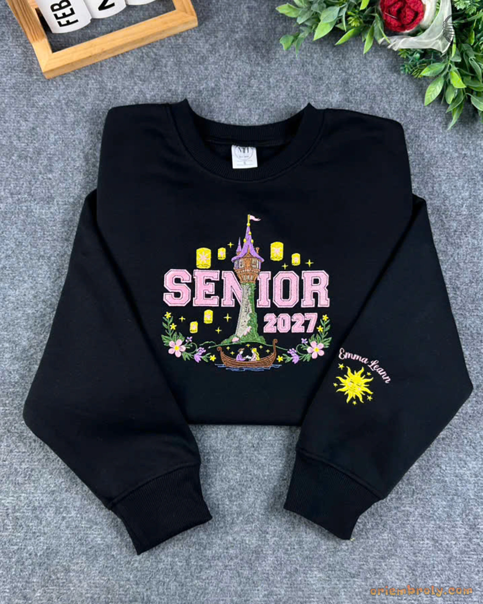 Flat lay of a black Senior 2027 sweatshirt featuring Tangled Rapunzel tower, floating lanterns, and sun emblem sleeve embroidery