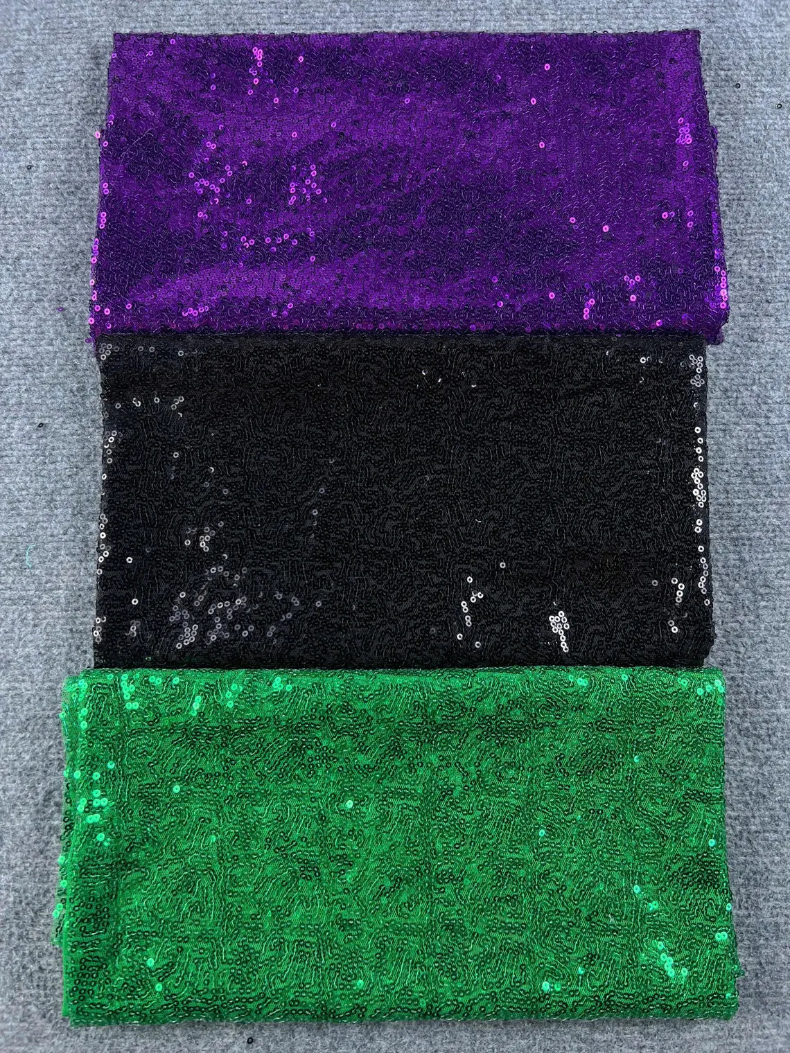 Close-up texture of purple, black, and green sequin sparkle fabric swatches for custom patches