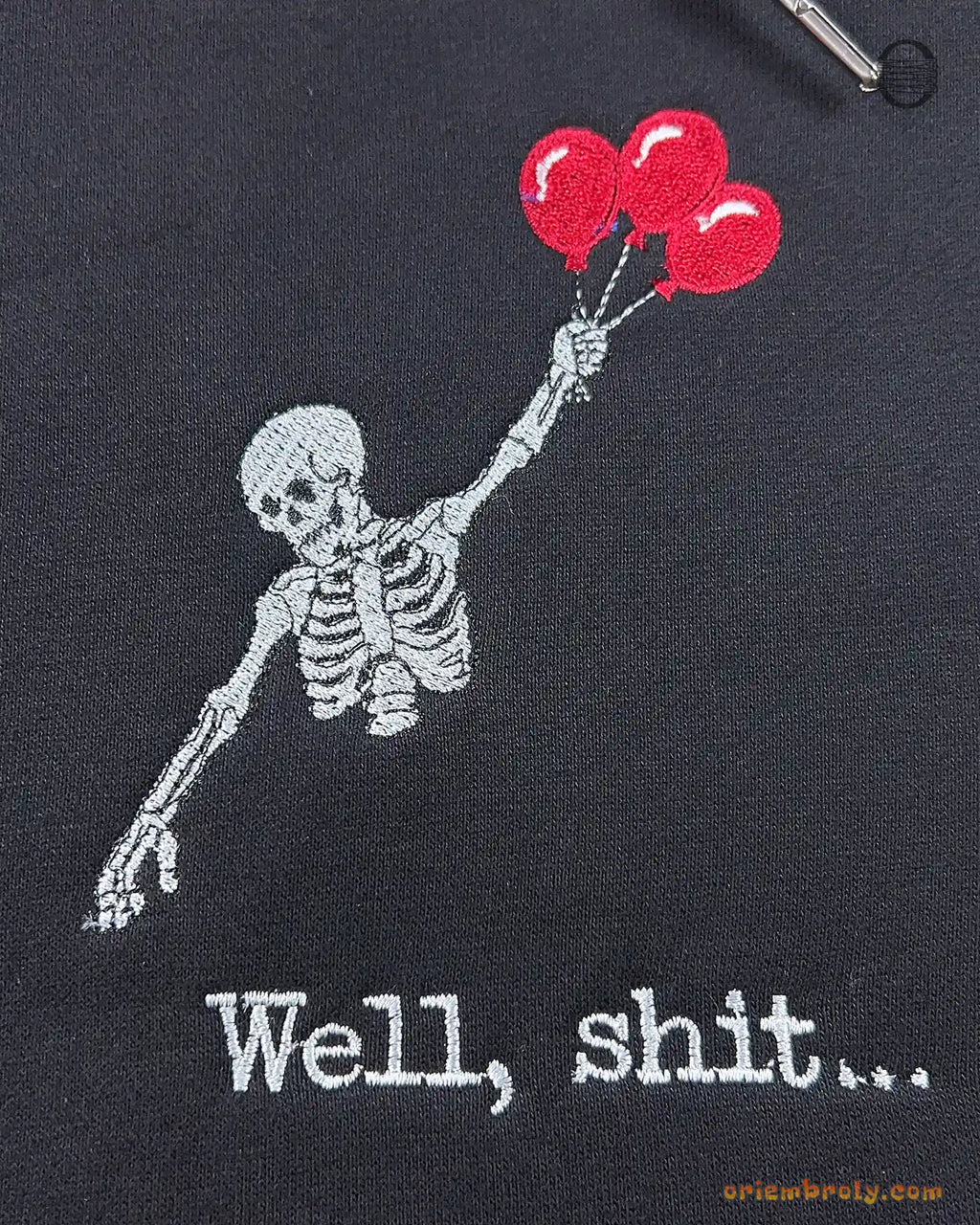 Close-up of upper skeleton body floating with red heart balloons and Well shit embroidered quote on a black hoodie