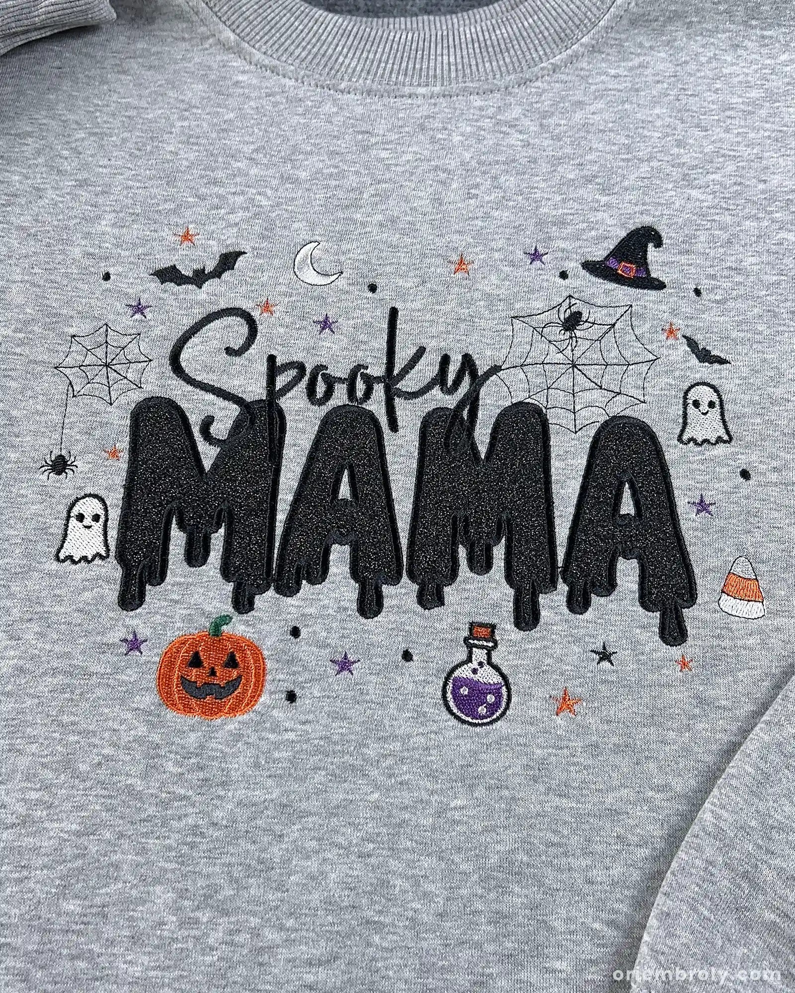 Close-up of Spooky MAMA embroidery on a gray sweatshirt featuring dripping font, witch hat, pumpkin, and ghost icons.