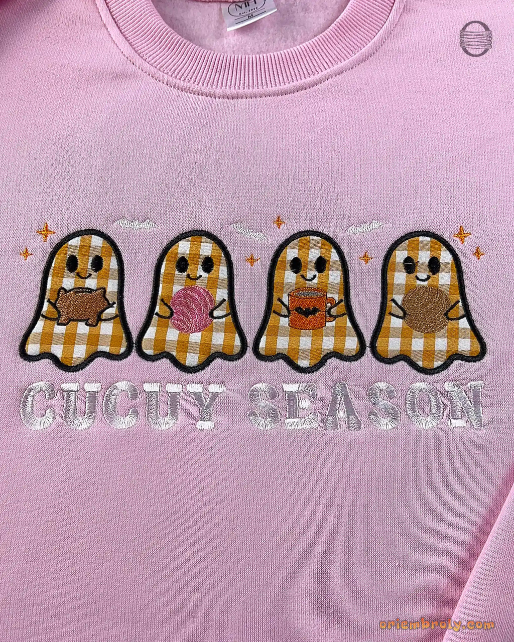 Close-up of Spooky Season applique embroidery with cute orange, brown, and pink plaid ghosts on a light pink sweatshirt