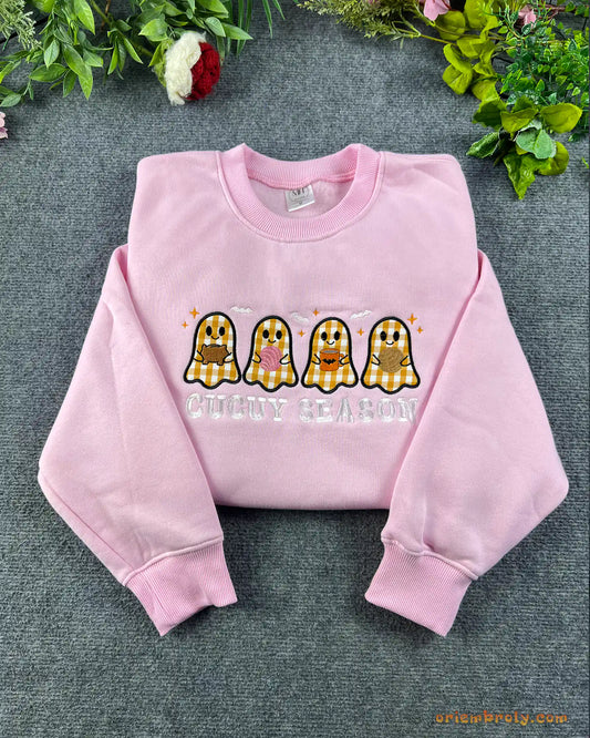Flat lay of a light pink crewneck sweatshirt embroidered with Spooky Season text and four cute plaid pattern ghosts
