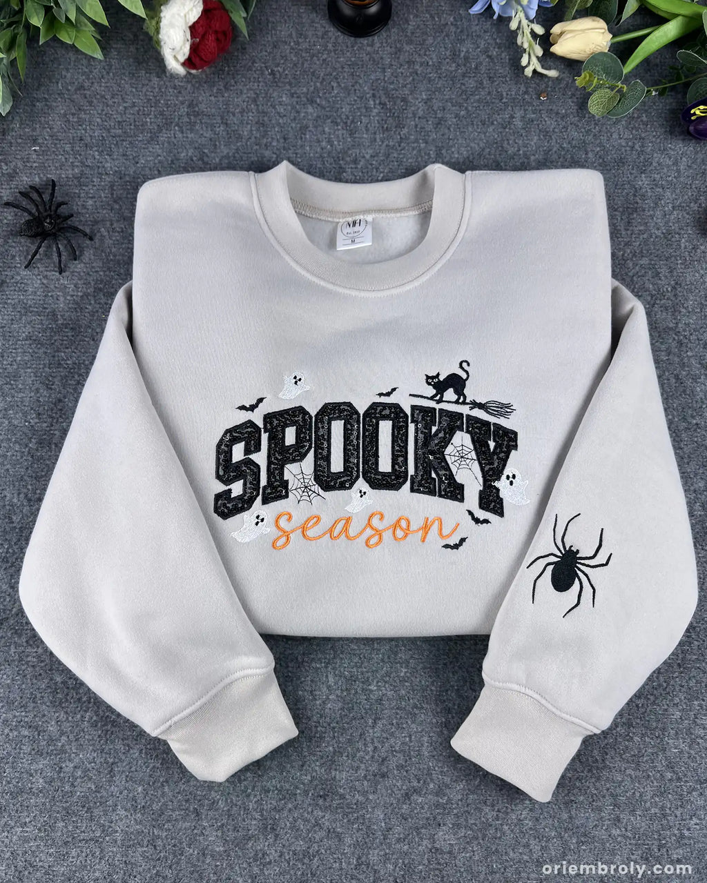Flatlay view of sand beige spooky season halloween embroidered crewneck sweatshirt with sleeve spider detail.