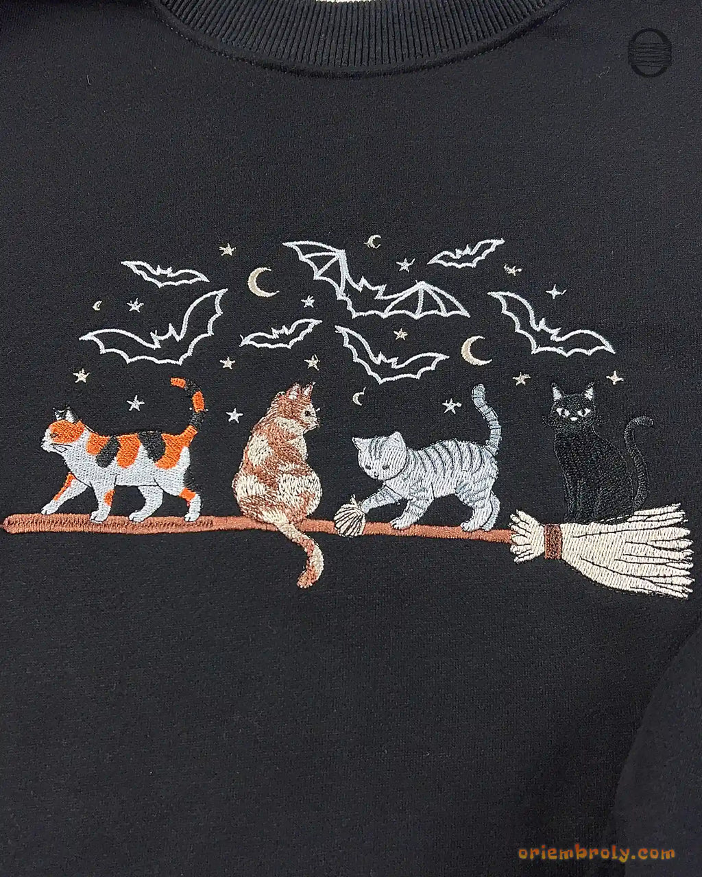 Close-up of Halloween witch cats riding a broomstick embroidery with bats and full moon on a black sweater