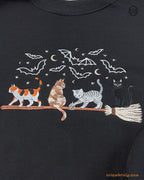 Close-up of Halloween witch cats riding a broomstick embroidery with bats and full moon on a black sweater