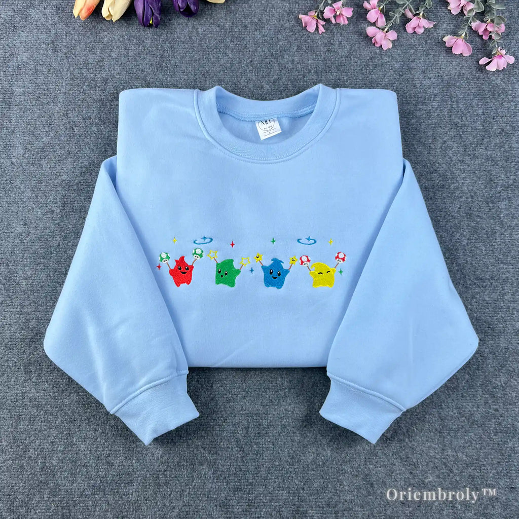 Light blue Stardew Valley sweatshirt featuring a row of colorful rainbow Junimo embroidery.