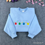 Light blue Stardew Valley sweatshirt featuring a row of colorful rainbow Junimo embroidery.