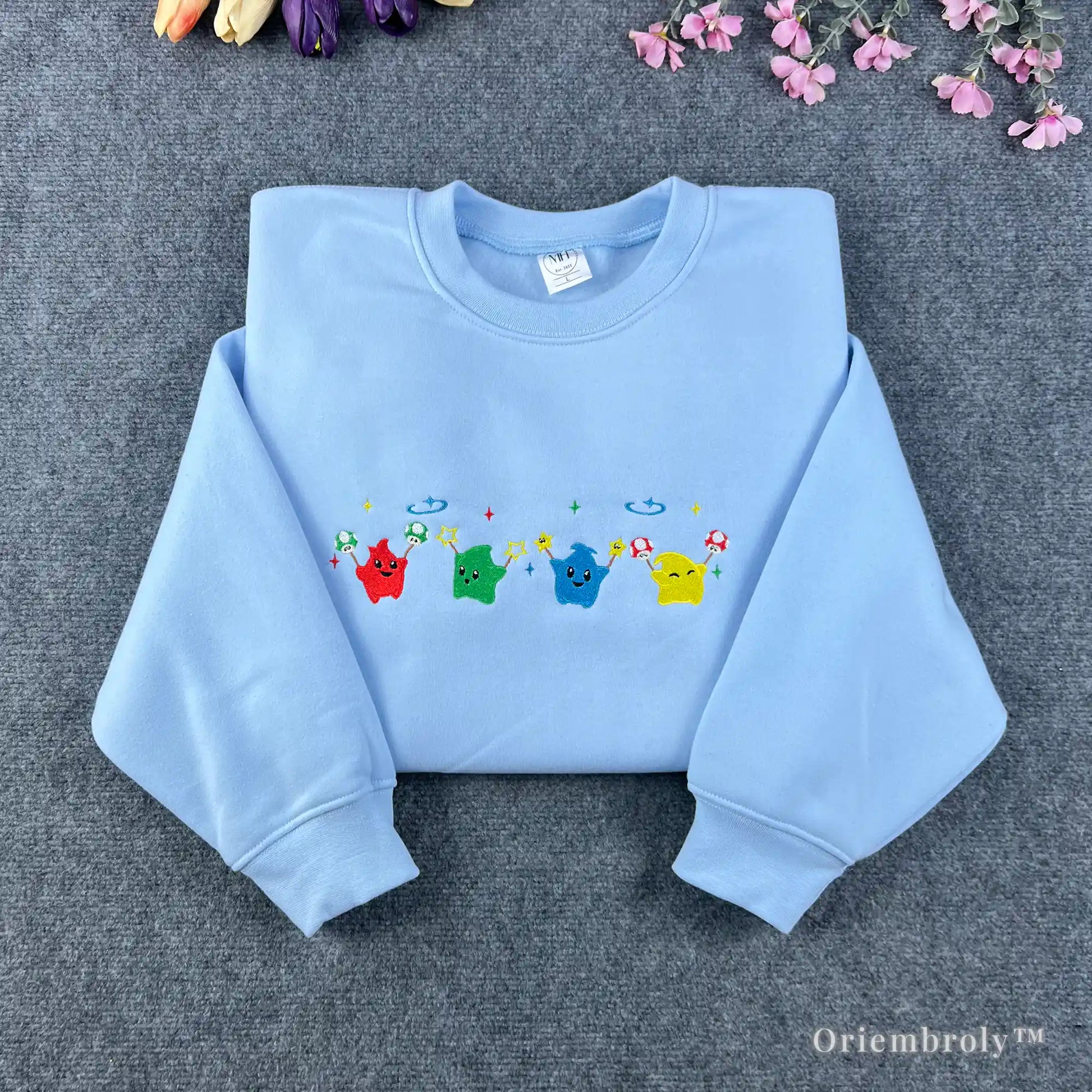 Light blue Stardew Valley sweatshirt featuring a row of colorful rainbow Junimo embroidery.