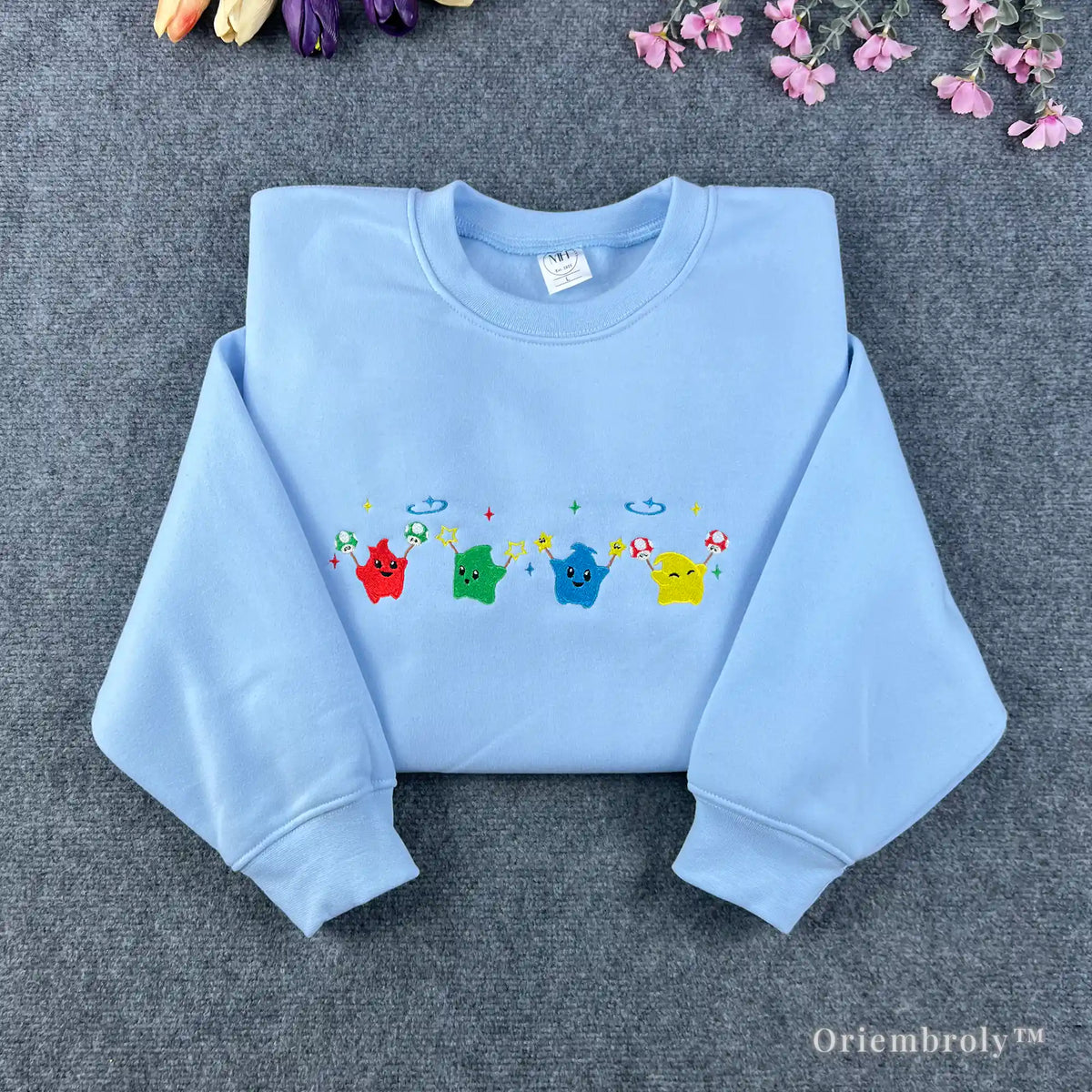 Light blue Stardew Valley sweatshirt featuring a row of colorful rainbow Junimo embroidery.