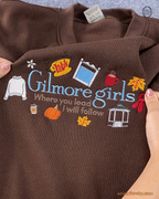 Detailed view of Stars Hollow coffee cup and gazebos embroidery on a dark brown crewneck sweatshirt