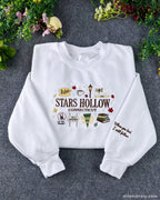 Flatlay view of a white crewneck sweatshirt embroidered with Stars Hollow Connecticut text, autumn icons, and custom sleeve embroidery.