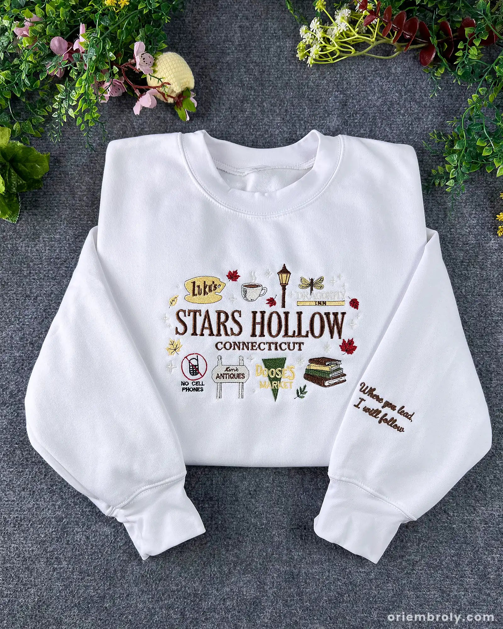 Flatlay view of a white crewneck sweatshirt embroidered with Stars Hollow Connecticut text, autumn icons, and custom sleeve embroidery.