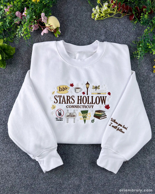 Flatlay view of a white crewneck sweatshirt embroidered with Stars Hollow Connecticut text, autumn icons, and custom sleeve embroidery.