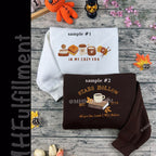 Two sweatshirts with printed designs on a wooden surface with decorative items.