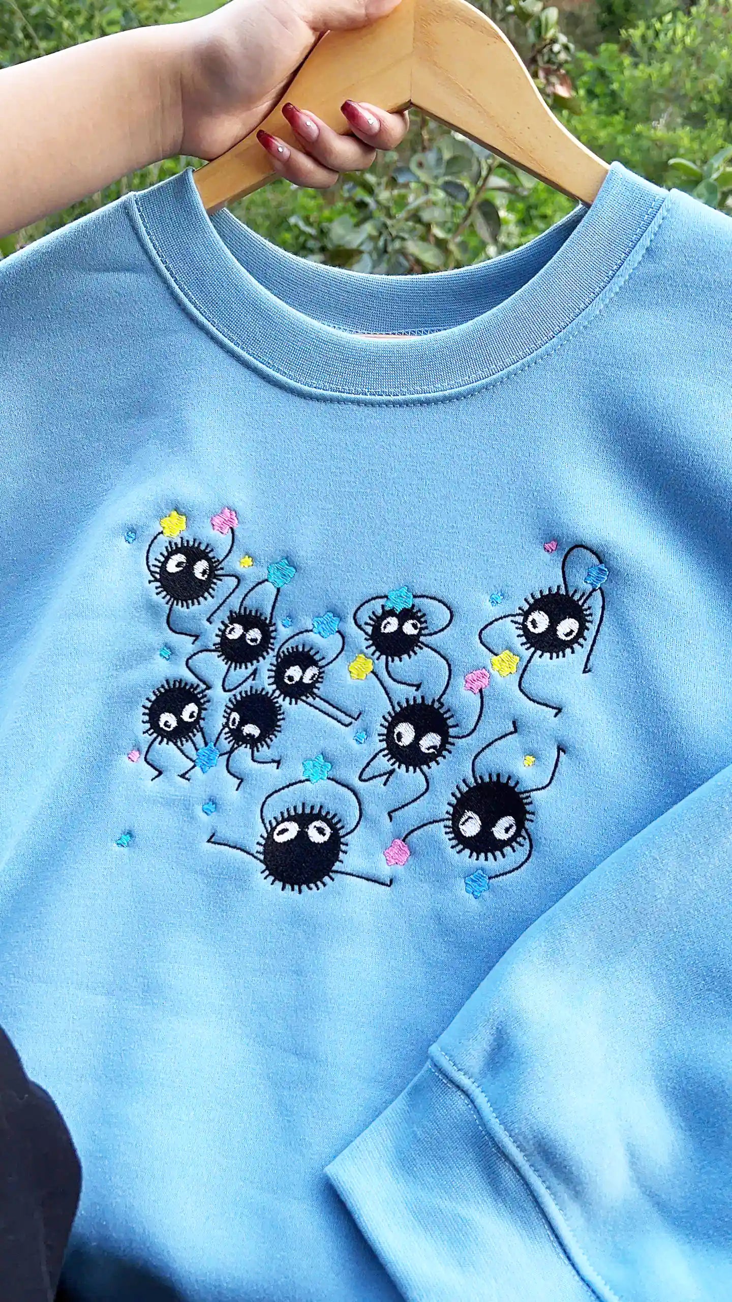 Blue sweatshirt with cartoon character design held by a hand on a blurred natural background