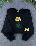Flat lay of a black embroidered sweatshirt featuring the golden Sundrop flower from Tangled with floating lanterns on the sleeve