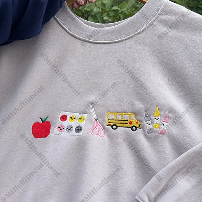 Gray sweatshirt with various embroidered designs including an apple, school bus, and other elements.