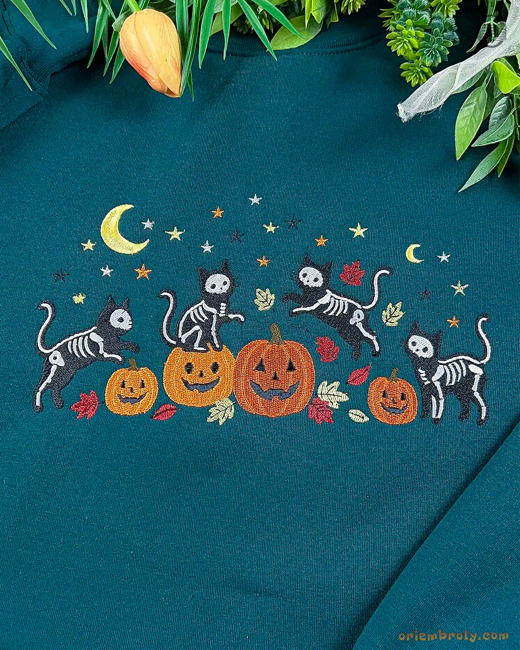 Detailed view of the embroidered design featuring black skeleton cats playing around orange pumpkins under a yellow crescent moon.