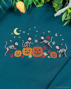 Detailed view of the embroidered design featuring black skeleton cats playing around orange pumpkins under a yellow crescent moon.