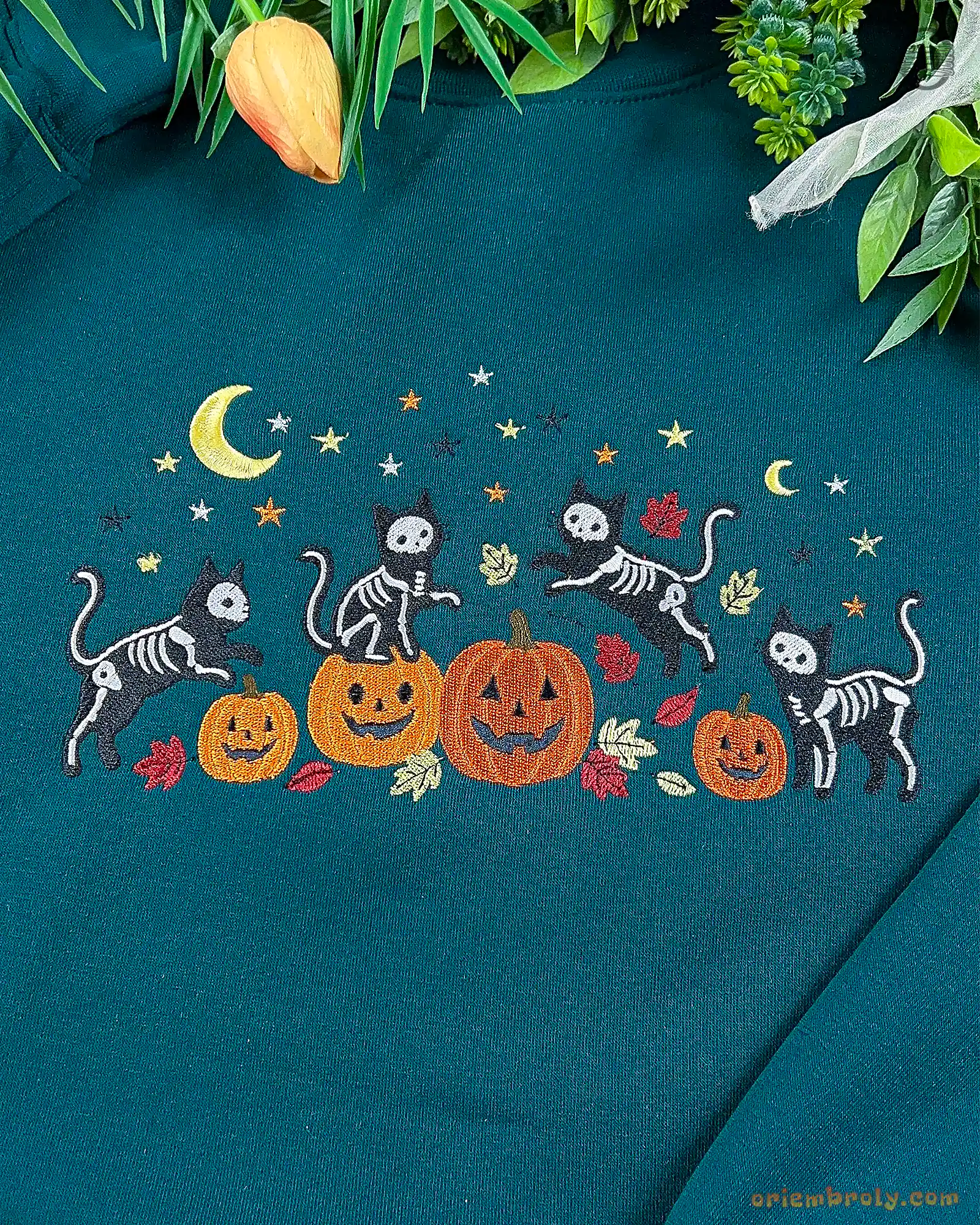 Detailed view of the embroidered design featuring black skeleton cats playing around orange pumpkins under a yellow crescent moon.