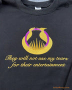 Close-up of gold embroidered quote They will not see my tears for their entertainment with Hunger Games emblem on a black sweater