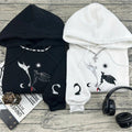 Black and white hoodies with dragon designs on a wooden surface with headphones and a magazine.