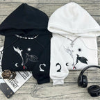 Black and white hoodies with dragon designs on a wooden surface with headphones and a magazine.