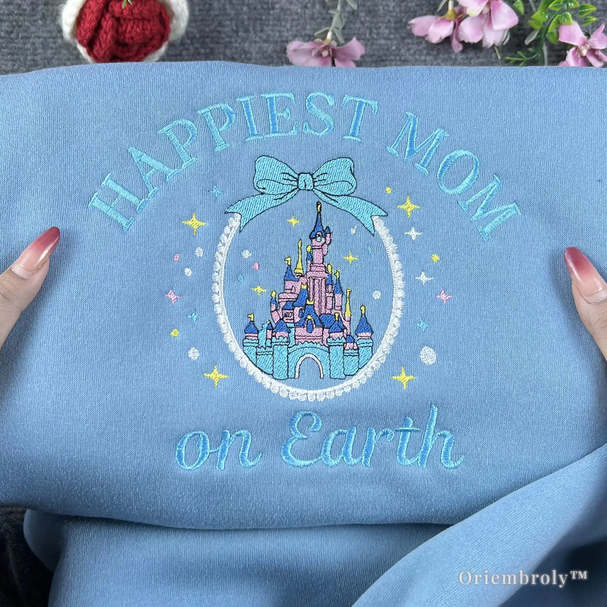 A high-quality embroidered Disney Mom hoodie in pastel blue. Featuring a fairytale castle and "Happiest Mom on Earth" script, it makes a thoughtful and unique gift for Disney-loving moms