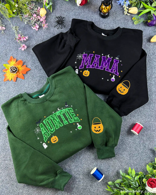 Flatlay setup of green Auntie and black Mama Halloween sweatshirts featuring sequin varsity lettering with autumn decorations.