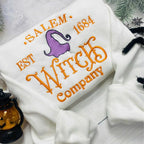 White sweatshirt with embroidered text and witch hat design on a light background.