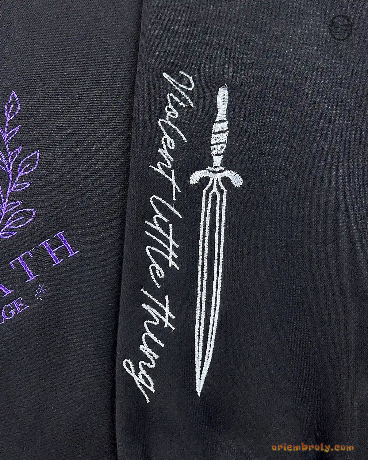 Close-up of silver dagger and Violence quote embroidered on the left sleeve of a black Basgiath War College sweatshirt