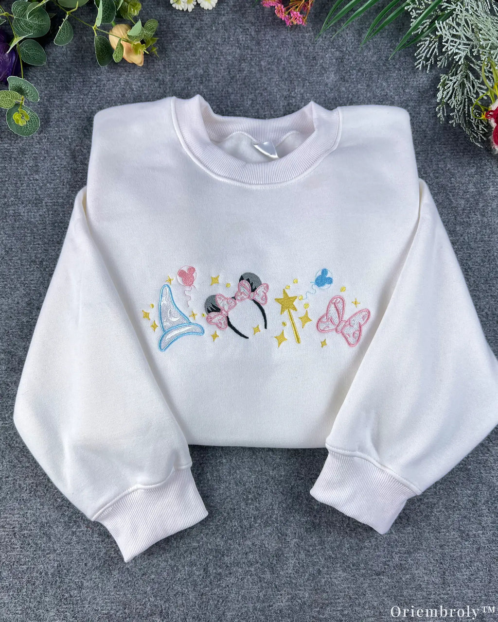 Flat lay of a white magical embroidered sweatshirt featuring Minnie mouse ears headband, princess crown, magic wand, and bow