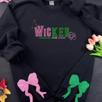 Black hoodie with 'Wicked Changed for Good' text and decorative bows on a dark background.