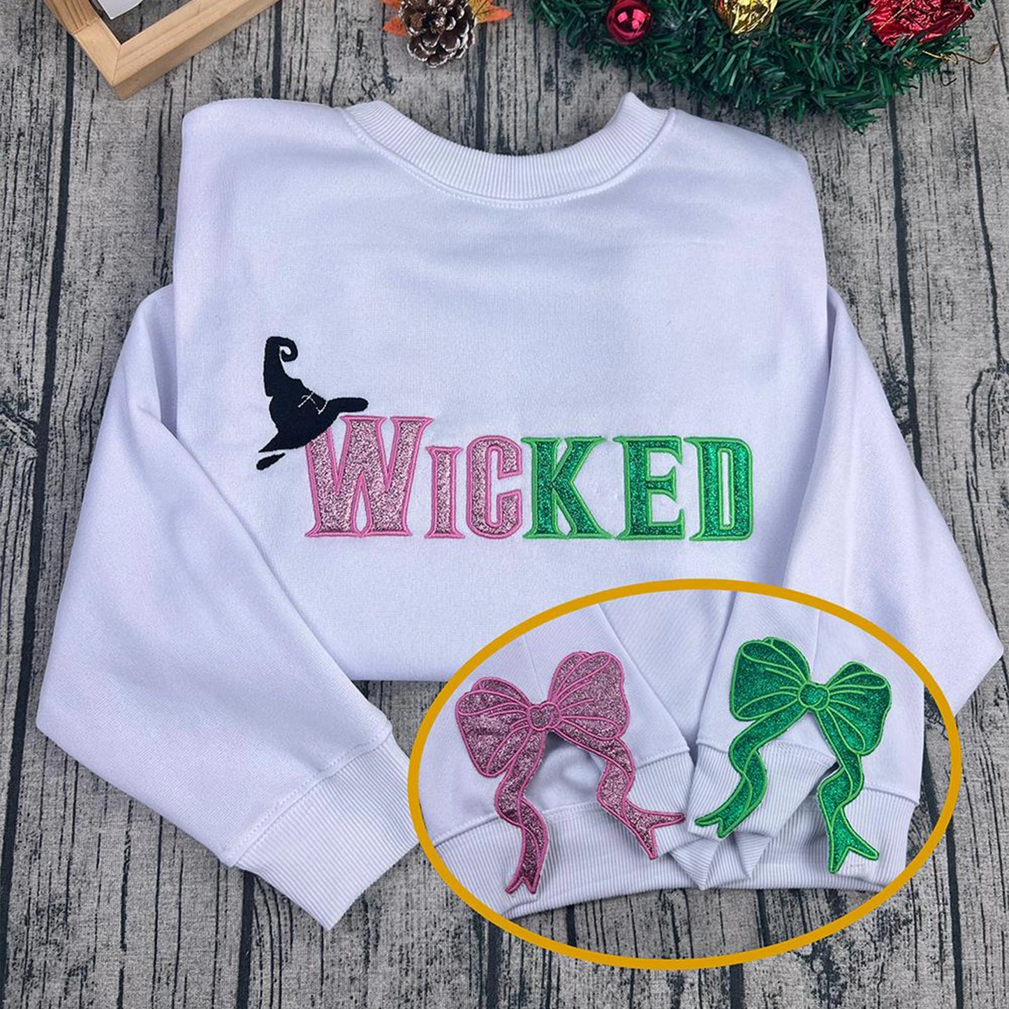 Wicked Glitter Embroidered Sweatshirt featuring an appliqué design inspired by the Wizard of Oz and Defying Gravity. A perfect Broadway fan gift.