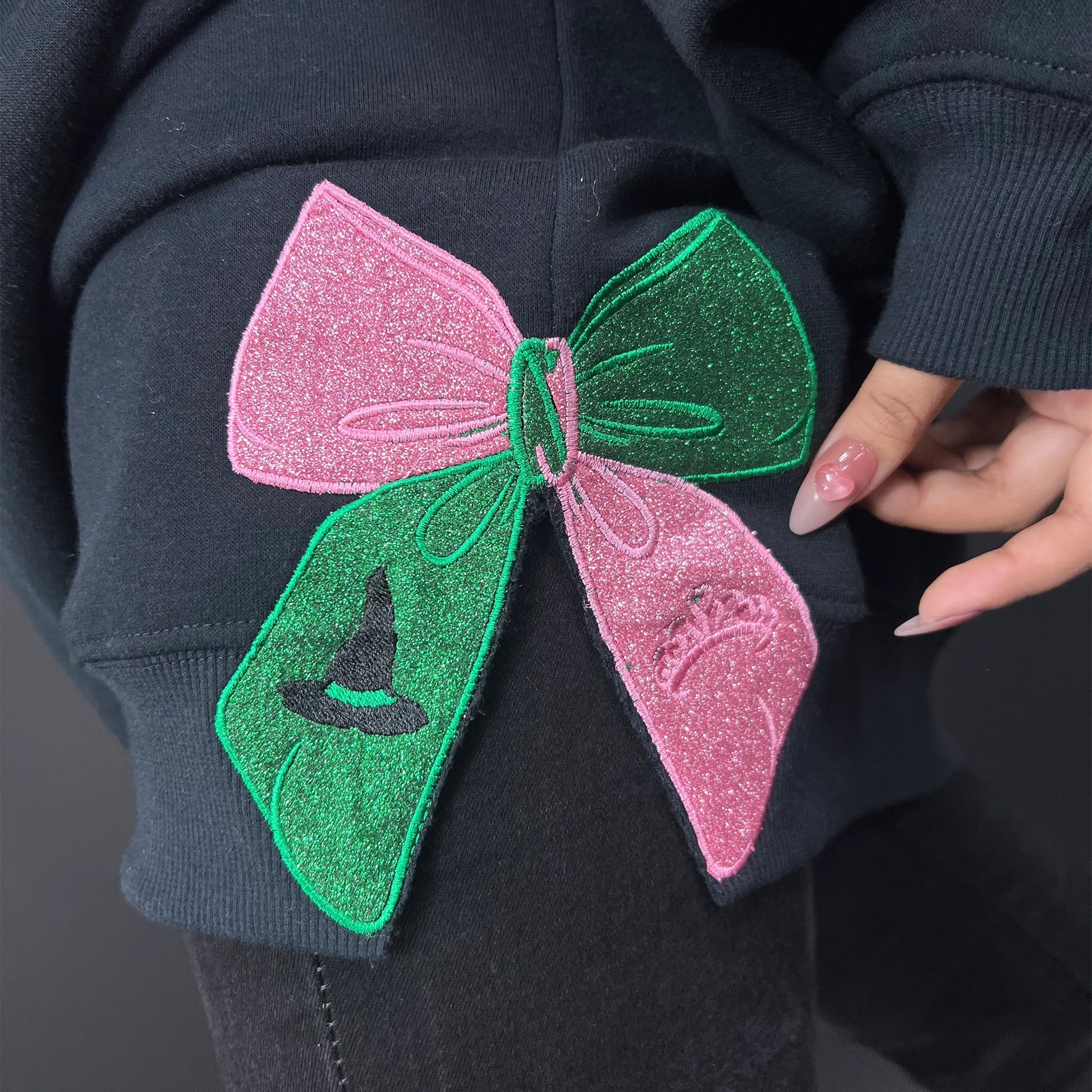 Wicked Movie embroidered sweatshirt featuring Defying Gravity design, side bow embroidery, and inspired by Glinda and Elphaba. Cozy and stylish for Broadway fans.