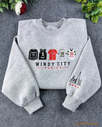 Flat lay of a heather grey crewneck sweatshirt embroidered with Windy City Series sports jerseys and Chicago skyline sleeve