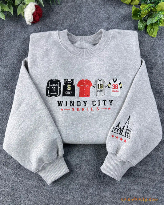Flat lay of a heather grey crewneck sweatshirt embroidered with Windy City Series sports jerseys and Chicago skyline sleeve