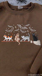 Detailed view of embroidered calico and black cats on a magic broomstick on a chocolate brown sweatshirt