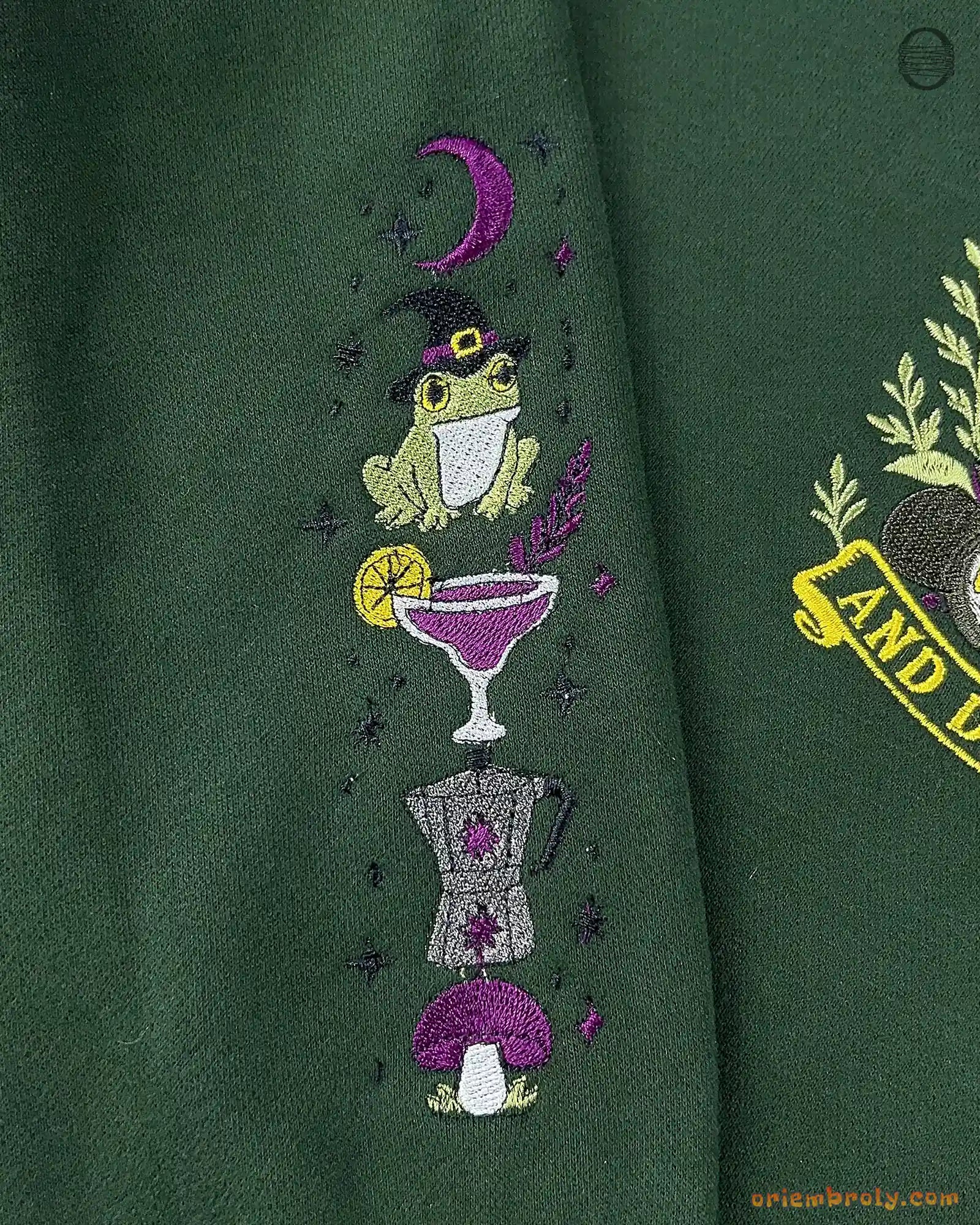 Close-up of wizard frog wearing hat and margarita cocktail sleeve embroidery on a forest green sweater