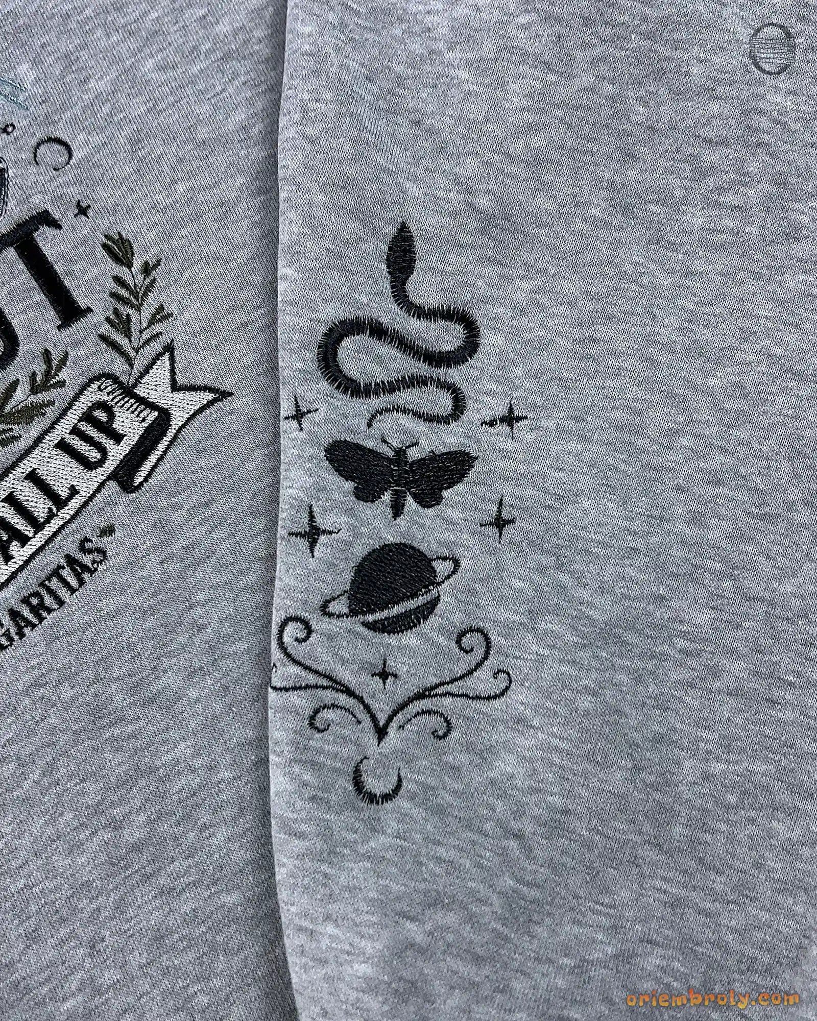 Close-up of witchy sleeve embroidery featuring a snake, moth, and celestial graphics on a grey sweater sleeve